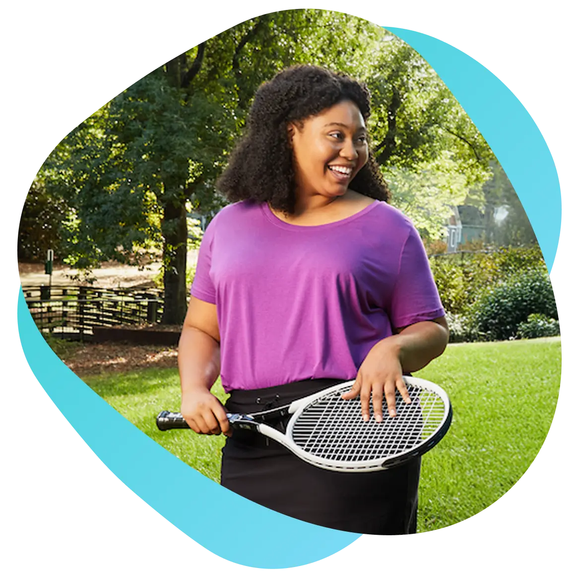 A woman stands outdoors, confidently holding a tennis racket in her right hand, ready to play